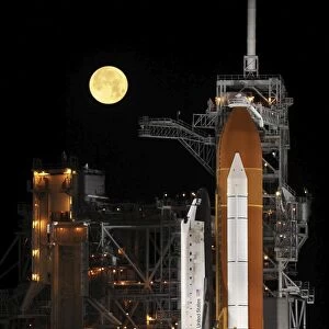 A nearly full Moon sets as Space Shuttle Discovery sits atop the launch pad