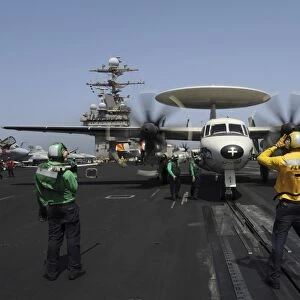 A plane director guides an E-2C Hawkeye onto the catapult for launch