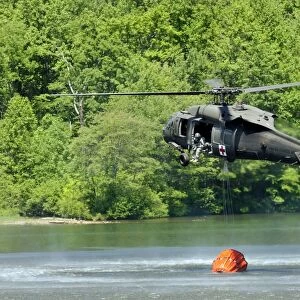 A UH-60 Blackhawk helicopter fills a suspended water bucket in Marquette Lake, Pennsylvania