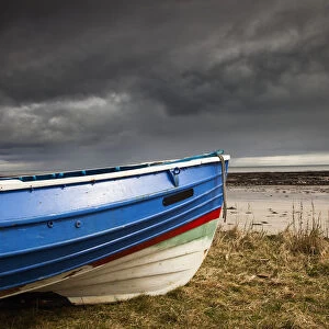 A Colourful Rowboat On The Shore With Dark Storm Clouds Overhead; Boulmer, Northumberland, England