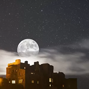 Full Moon Glowing In A Starry Sky Over Illuminated Buildings; Bamburgh, Northumberland, England