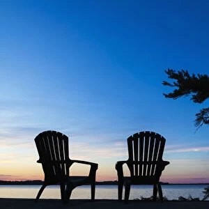 Silhouette Of Muskoka Chairs And Balsam Lake At Sunrise; Ontario, Canada