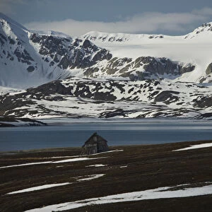 Small Wooden Cabin On The Shore Of The Arctic Ocean And Snow Covered Mountains; Spitsbergen, Svalbard, Norway
