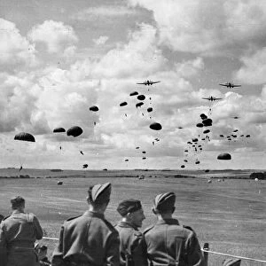 British army soldiers watch paratroops descending from aircraft during a demonstration in