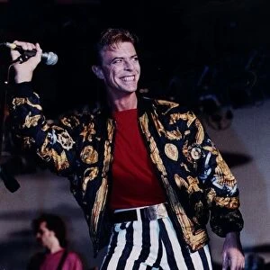 David Bowie singer on stage mike in hand wearing black and white striped trousers red