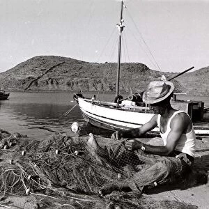 fisherman tends to his nets in Greece - fishing boat mountains river