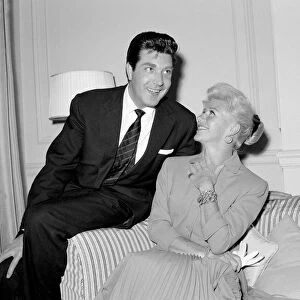 Ginger Rogers sitting on a couch laughing with David Hughes May 1959