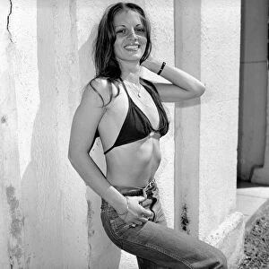 A glamour model wearing a bikini top and jeans April 1975