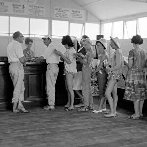 Holidaymakers line up to make a bet at a betting shop in the form of a wooden chalet
