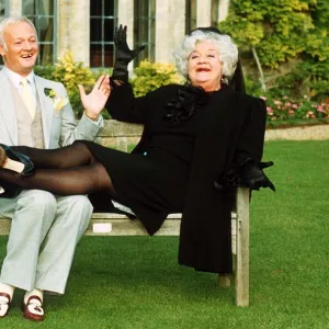 John Inman Comedy Actor and Mollie Sugden Comedy Actress sitting on wooden bench seat in