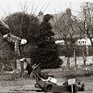A man mowing his lawn with doing a hand stand on the handles of an electrical lawn mower
