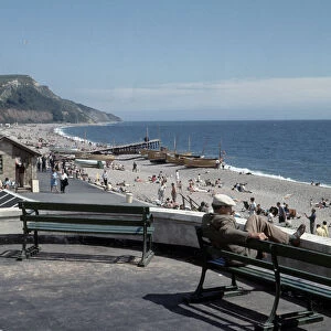 A man sitting on bench looks out over the beach at the small seaside town of Seaton