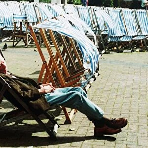 Man sleeping on deckchair in a London park on windy day