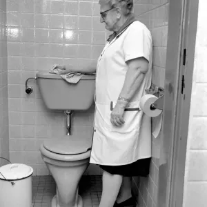 Print of an elderly woman cleaning a toilet, November 1969 Print of an elderly woman cleaning a toilet, November 1969