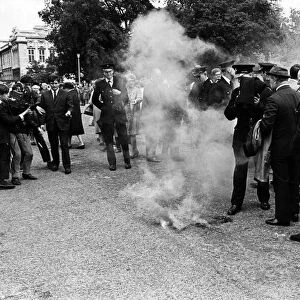 A police officer (centre) prepares to throw his cloak over a smoke bomb hurled as Prince