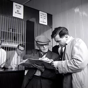 Punters studying the form guide before placing a bet at William Massey betting shop in