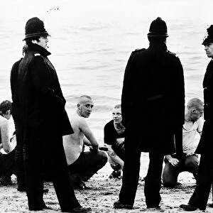 Skinheads sitting on the beach surrounded by the Police
