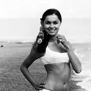 Virginia North modelling a bikini on a beach staning with her hand on her hip smiling