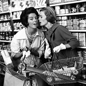Two women whisper to each other in aisle of shop, 9th September 1960