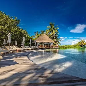 Luxury beach swimming pool at sunset with reflection of palm trees, tropical landscape, exotic island hotel. Loungers and chairs with closed umbrella