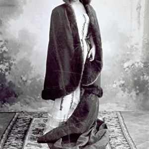 Full-length portrait of a young woman wrapped in a fur stole. On the floor there is an elaborately worked carpet