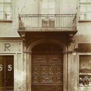 View of the doorway to a building in Turin flanked by shop windows and shops. Over the doorway a simple balcony in wrought iron