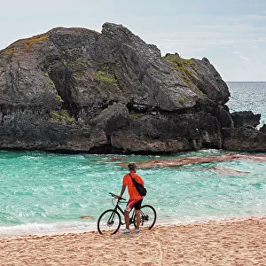 Bermuda, Warwick Long Bay, cyclist standing on beach with aquamarine water and pink sand