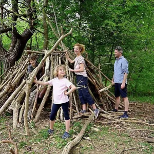 Girl holding log while building camp with family in forest
