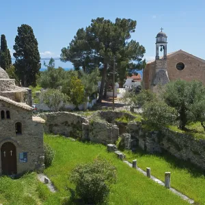 Old church surrounded by ruins in a rural area with tall cypress trees