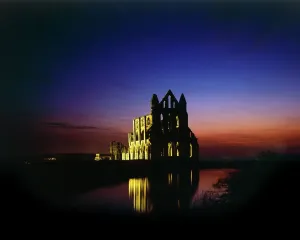 Prints of WHITBY ABBEY, North Yorkshire. A floodlit view of the abbey at night with reflection in the water North Yorkshire Prints: Whitby Abbey Nighttime Print