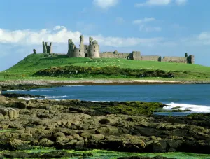 Prints of DUNSTANBURGH CASTLE, Northumberland. View of the castle with rocks and sea in the foreground Castle Prints: Dunstanburgh Castle Print, a photograph of the castle and coastline