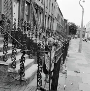 House And Home Prints: Print of an elderly woman sweeping steps in front of a terraced house