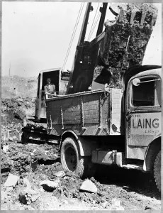 Prints of FILTON AIRFIELD, SOUTH GLOUCESTERSHIRE. A dragline excavator depositing material from a bucket into a flatbed van during the construction of a new runway at Filton Airfield Engineering And Construction Prints: Loading a lorry Print, black and white photograph