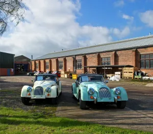 Prints of Morgan Motor Company, Pickersleigh Road, Malvern, Worcestershire. Two Morgan cars with factory beyond Worcestershire Prints: Morgan Factory Print DP139433