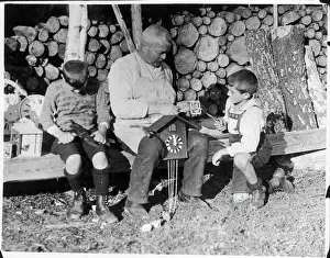 Prints of Two little boys help an old clockmaker, perhaps their grandfather, to make a cuckoo clock in the Black Forest, Germany Related Prints: Black Forest Cuckoo Clock Maker Print