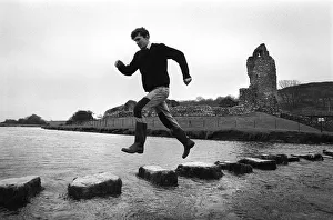 A man leaps along the stepping stones at Ogmore Castle A man leaps along the stepping stones at Ogmore Castle