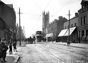Prints of Newtownards Rd. Belfast - a busy street scene with shop fronts, tram, people, horse vehicles and a cobbled road surface, and Church visible. (Location: Northern Ireland: County Antrim: Belfast) Newtownards Prints: Early 20th Century Print of Newtownards Rd, Belfast