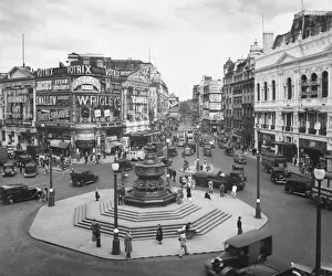 Prints of Piccadilly Circus and the Statue of Eros, London. The street scene is dominated by advertising hoardings and illuminations for Gordons Gin, Wrigleys Chewing Gum and others Piccadilly Circus Prints: Piccadilly Circus and the Statue of Eros, London Print 1930s