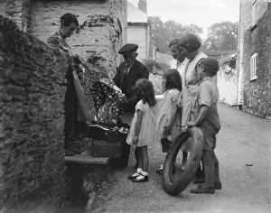 Prints of Mothers and children gather around the local rag and bone man with their various offerings on the back streets of Harbertonford, south Devon, England Harbertonford Prints: Rag and Bone Man Print, Harbertonford, South Devon