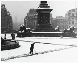 Prints of A man sweeps a path in the heavy snow at the base of Nelsons Column in Trafalgar Square. Note Landseers lions covered in snow Weather Prints: Snow Covered Trafalgar Square Print