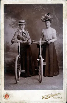 A splendid cabinet photograph of two well-dressed women standing proudly with their bicycles A splendid cabinet photograph of two well-dressed women standing proudly with their bicycles
