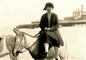 Woman perched on a wooden donkey at the seaside Woman perched on a wooden donkey at the seaside
