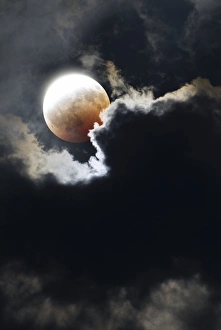 Prints of Partial lunar eclipse seen through clouds. The brightly lit portion of the Moon is still reflecting sunlight. The dimmer, orange portion of the Moon has passed into the shadow cast by the Earth Images Dated 2009 May: Partial Lunar Eclipse Print