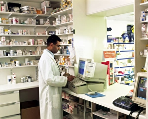 Prints of MODEL RELEASED. Pharmacist. View of a pharmacist using a computer to fill in a patient record form. This form details the various medications the patient has received from the pharmacy Images Dated 2003 September: Pharmacist Using a Computer Print
