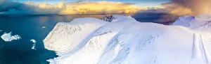 Aerial view of sunrise on snow capped mountains and blue arctic sea, Sorvaer Aerial view of sunrise on snow capped mountains and blue arctic sea, Sorvaer