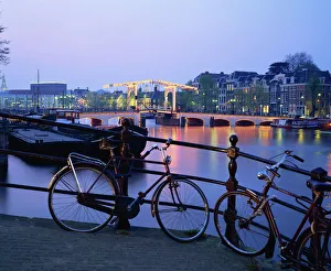 Prints of Bicycles by the side of the canal, with barges, and the Magere Brug (Skinny Bridge) in the background, in the evening in Amsterdam, Holland, Europe Amsterdam Prints: Evening Scene Print of Bicycles by Amsterdam Canal