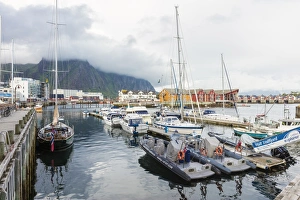 Clouds on rocky peaks frame the boats in the harbor of the fishing village of Svolvaer Clouds on rocky peaks frame the boats in the harbor of the fishing village of Svolvaer