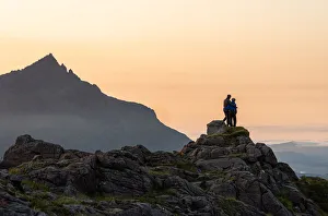 A couple standing on a rocky peak watching a mountain sunset with Sgurr nan Gillean in A couple standing on a rocky peak watching a mountain sunset with Sgurr nan Gillean in