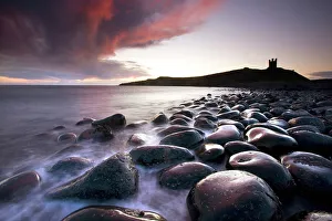 Dawn over Embleton Bay with basalt boulders in the foreground and the ruins of Dunstanburgh Castle in the background Dawn over Embleton Bay with basalt boulders in the foreground and the ruins of Dunstanburgh Castle in the background
