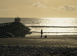 Fisherman on the beach silhouetted against the winter sun where the Arun estuary enters the sea Fisherman on the beach silhouetted against the winter sun where the Arun estuary enters the sea